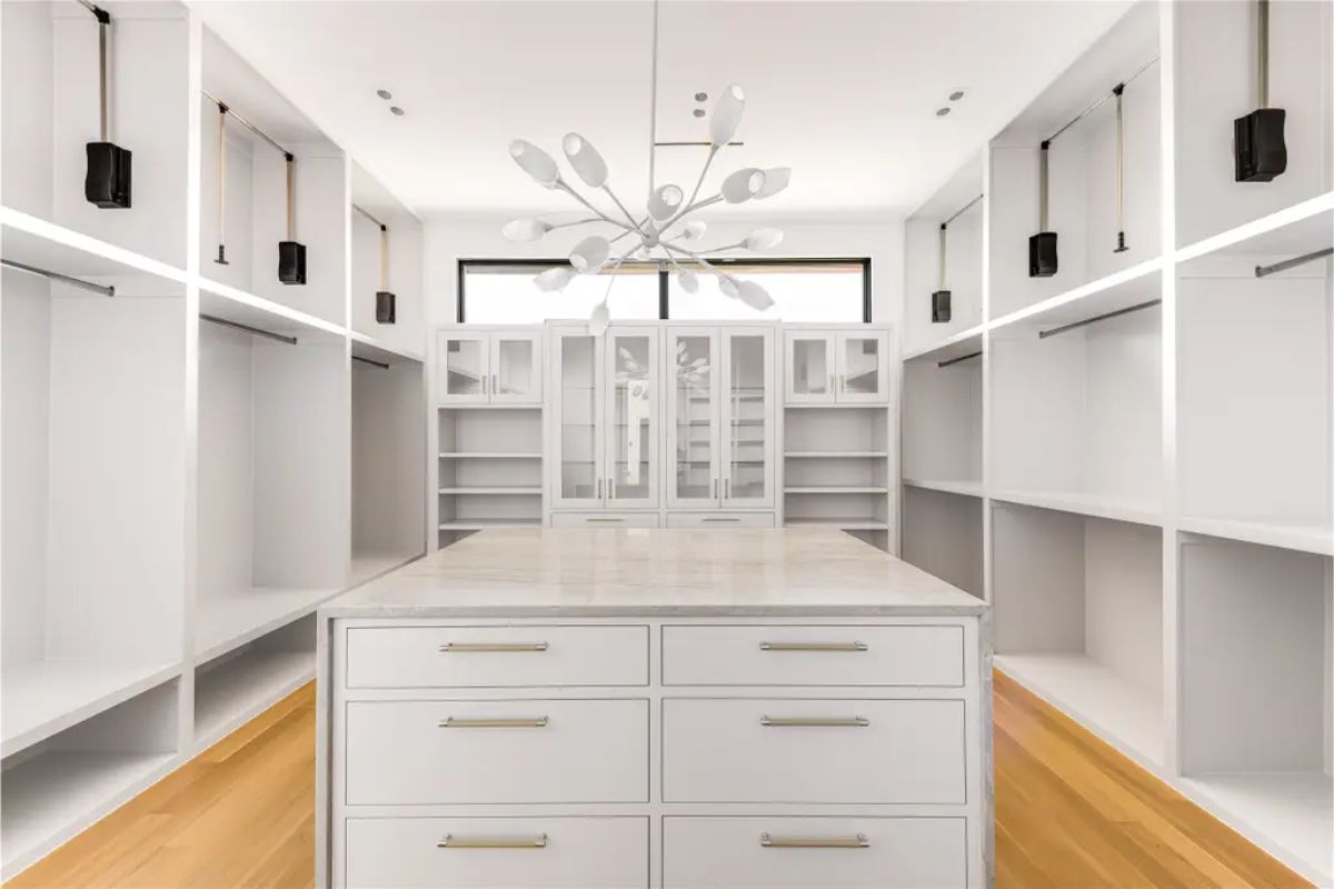 Elegant walk-in closet with built-in shelving, a central island with drawers, and a statement chandelier. 