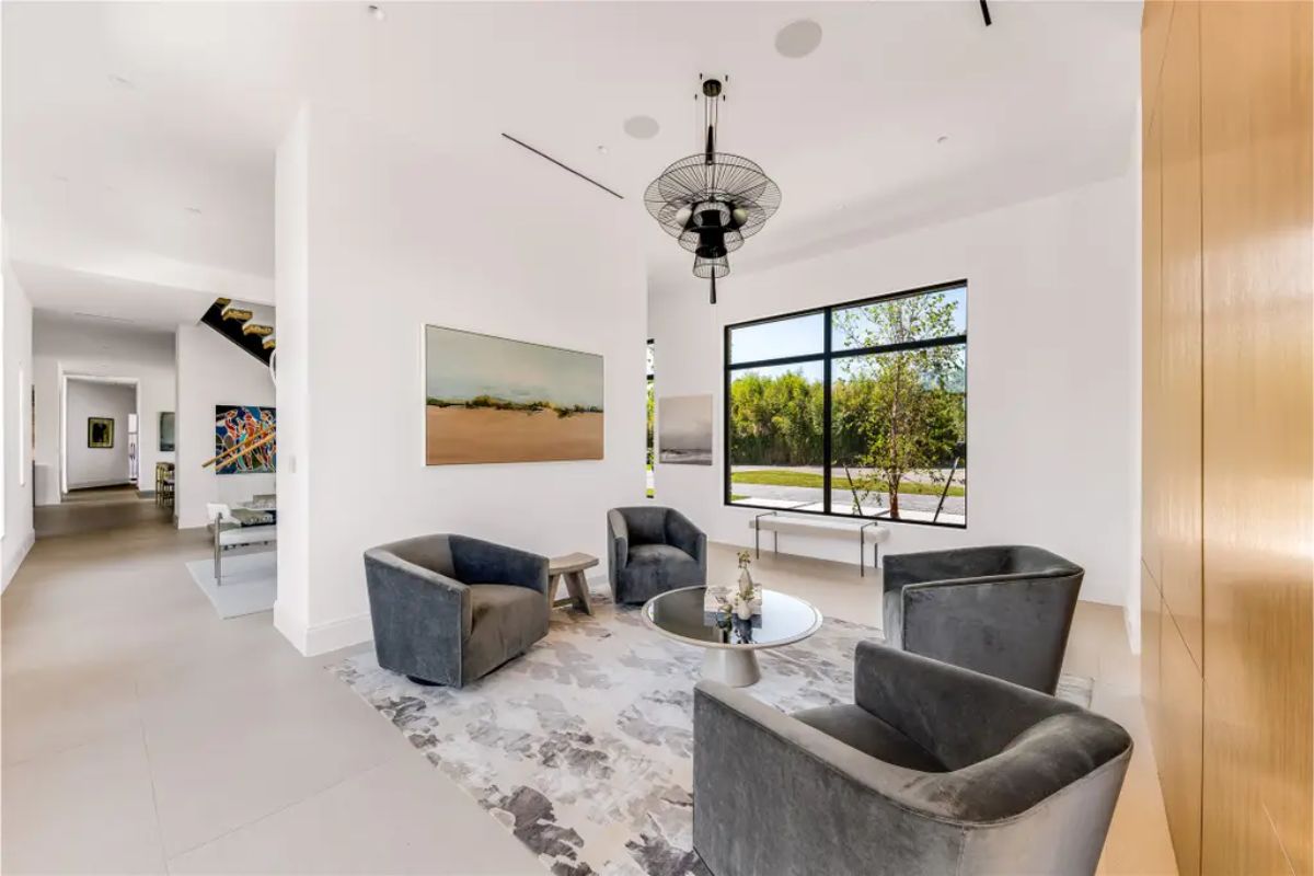 Secondary seating area with plush gray chairs, a contemporary chandelier, and a large window letting in natural light. 