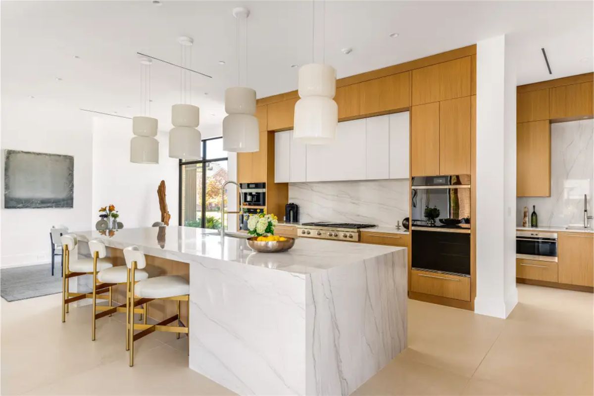 High-end kitchen featuring a waterfall marble island, custom wood cabinetry, built-in appliances, and pendant lighting. 