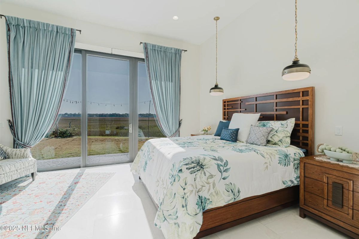Bright bedroom with a wooden bed frame and floral bedding facing full-length glass doors.