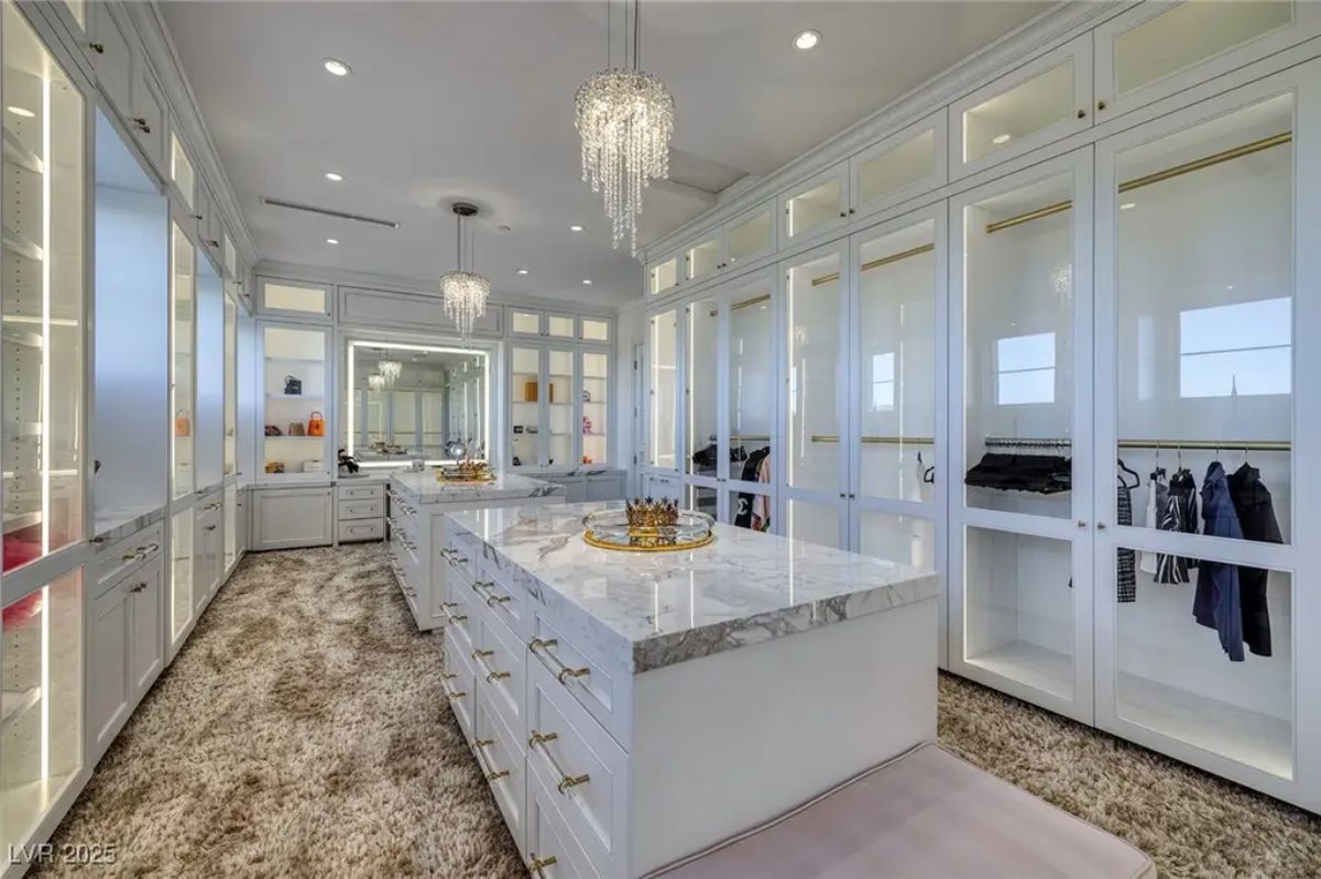 Walk-in closet with white cabinetry and glass doors showcases an organized wardrobe.