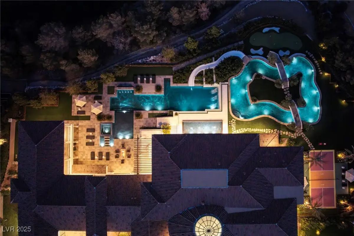 Nighttime aerial shot showcases the estate's expansive layout with multiple outdoor living spaces.