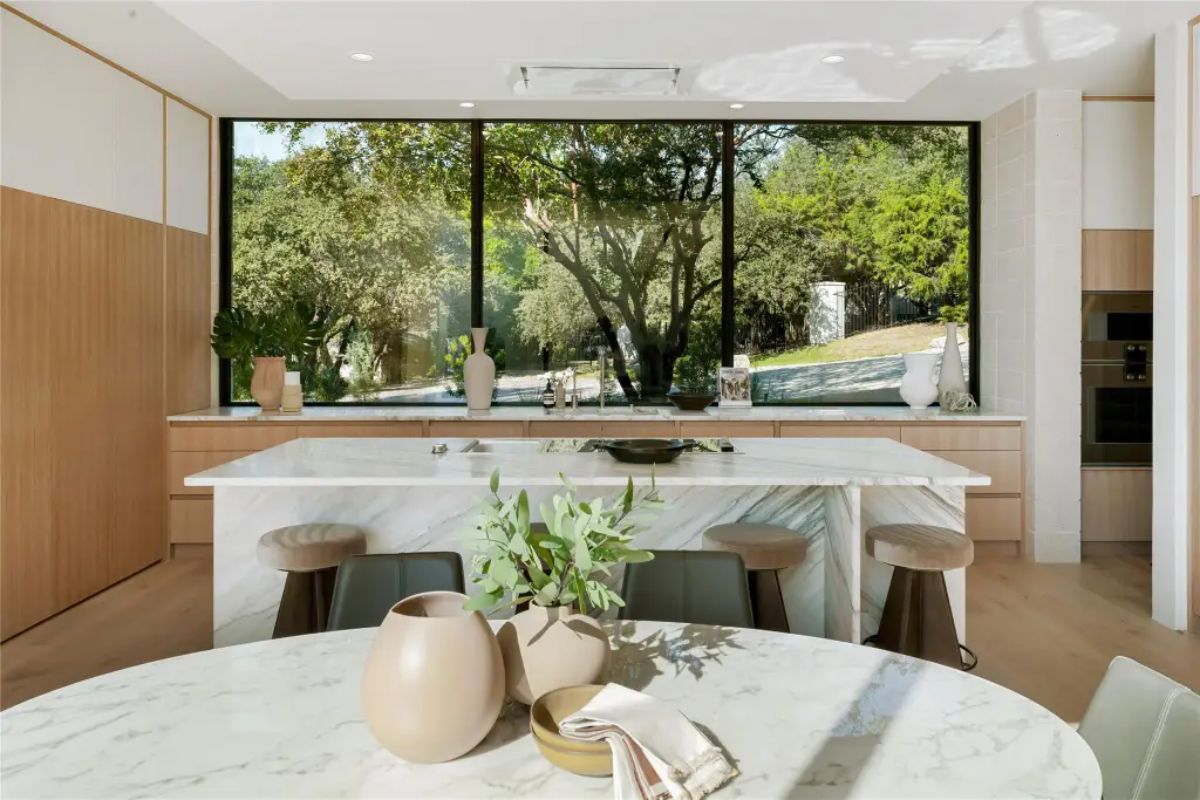 Sleek modern kitchen with a large island, marble countertops, and a scenic view through floor-to-ceiling windows. 