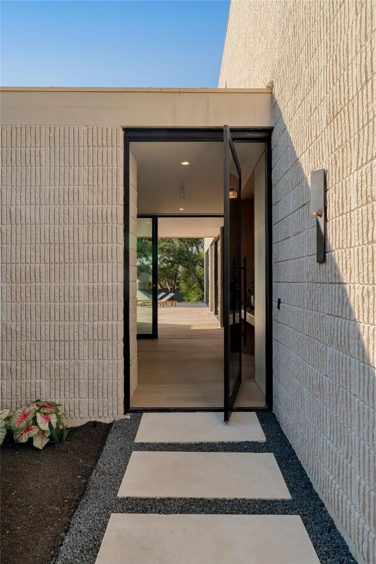 Elegant entryway with a sleek black-framed glass door, surrounded by textured walls and a minimalist pathway. 