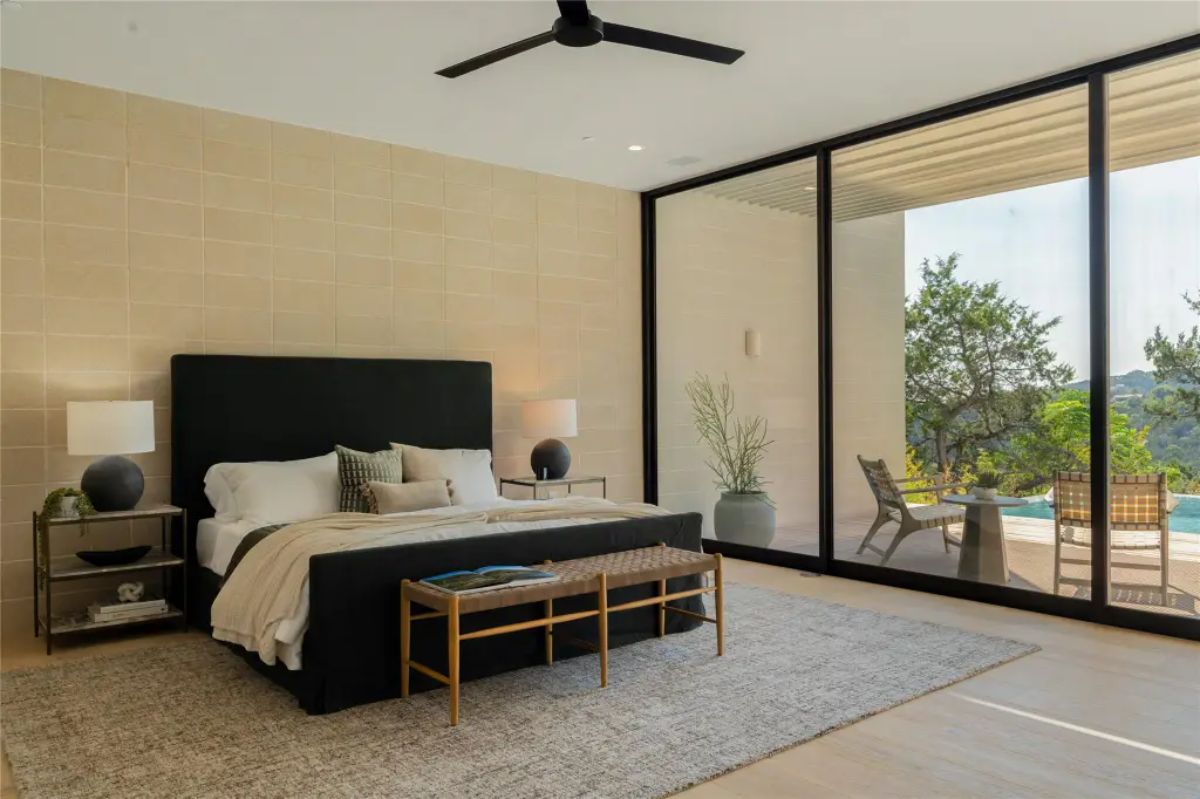 Spacious bedroom with a black upholstered bed, large windows, and direct access to an outdoor poolside patio. 