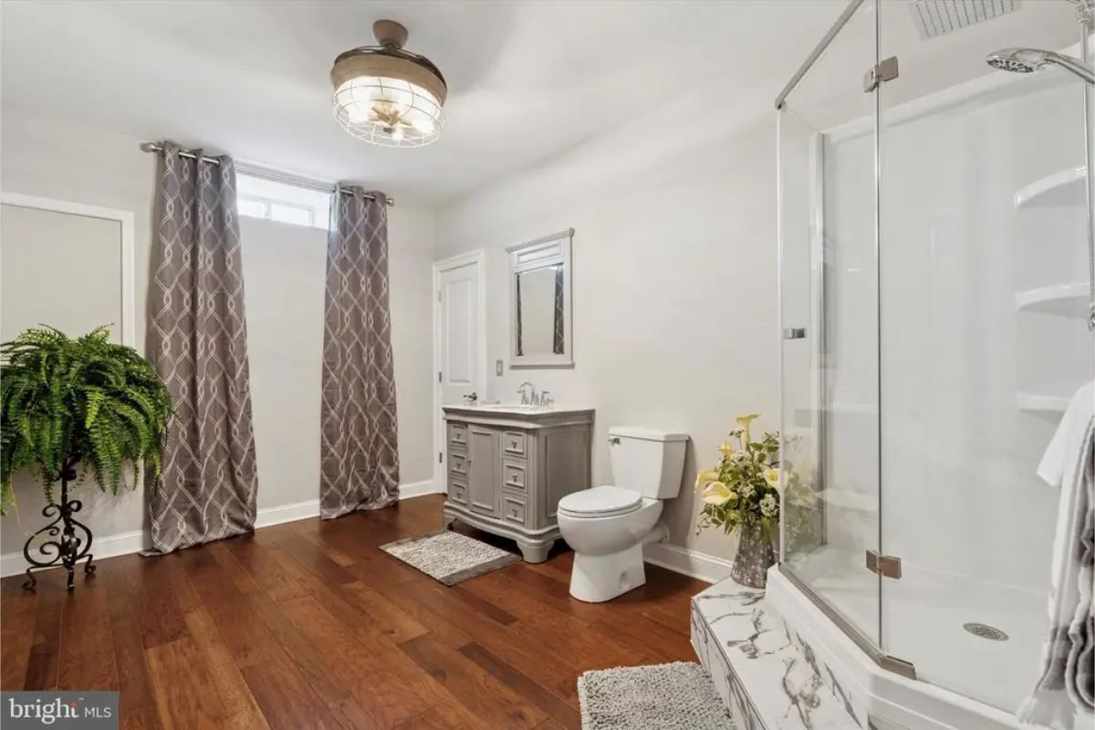 Glass-enclosed shower is positioned next to a freestanding vanity with storage.
