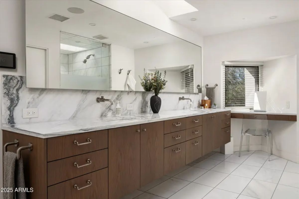 Elegant bathroom featuring a long marble countertop, dark wood cabinetry, and a skylight for natural lighting. 