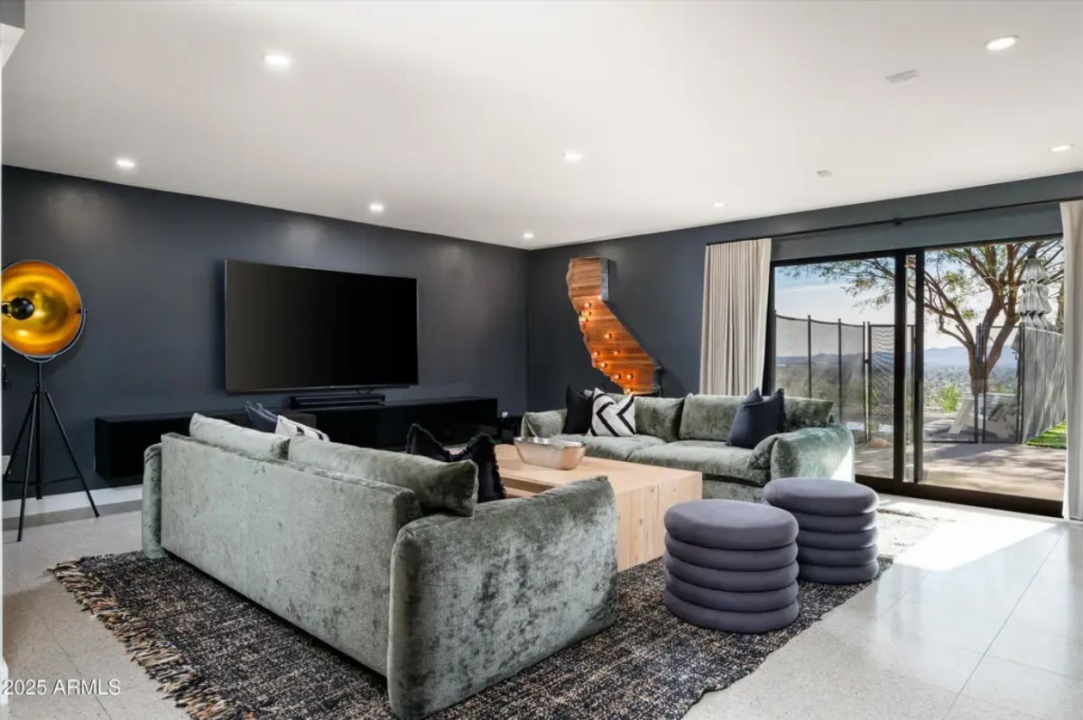 Cozy entertainment room with dark walls, plush velvet sofas, and sliding glass doors leading to an outdoor patio. 