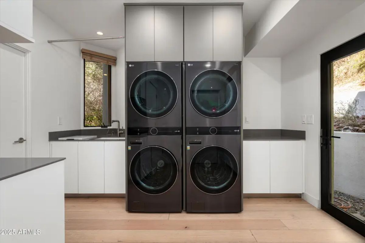 Spacious laundry room with double-stacked black washer-dryers, white cabinetry, and direct outdoor access. 