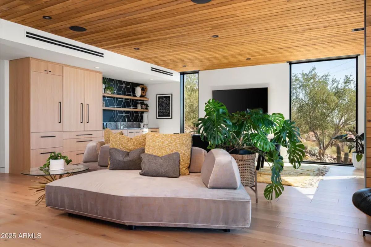 Stylish lounge area with a warm wooden ceiling, built-in shelving, and large windows overlooking the landscape. 