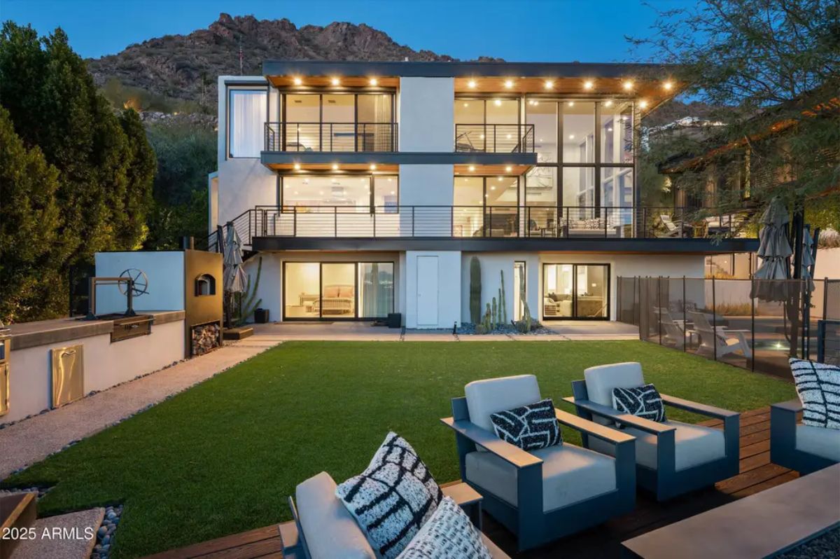 Rear exterior view of the modern multi-level home featuring large glass walls, sleek balconies, and an outdoor lounge. 