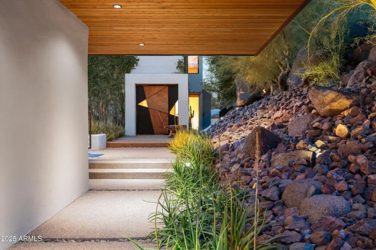 Unique entry pathway with a floating wooden ceiling, natural stone steps, and desert landscaping blending into the surroundings. 