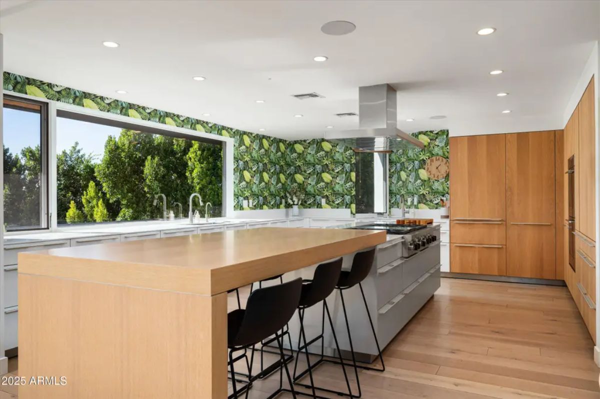 Spacious kitchen featuring a large wood island, botanical wallpaper, and sleek modern cabinetry. 