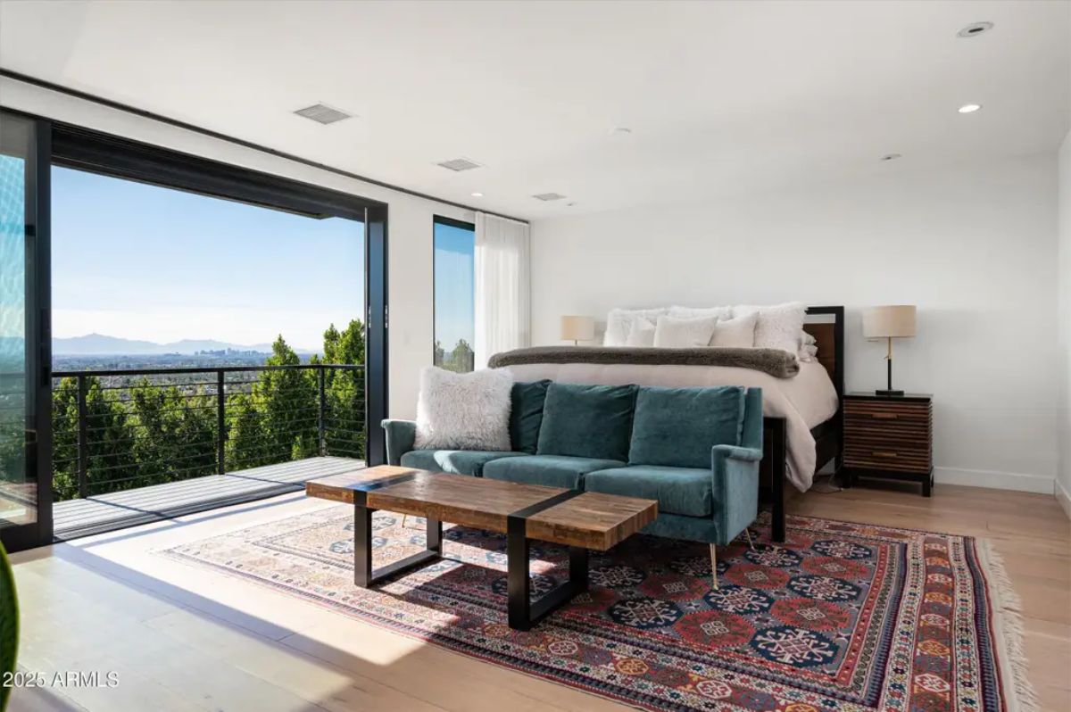 Master bedroom with a private balcony, large sliding doors, and an inviting seating area overlooking lush greenery. 