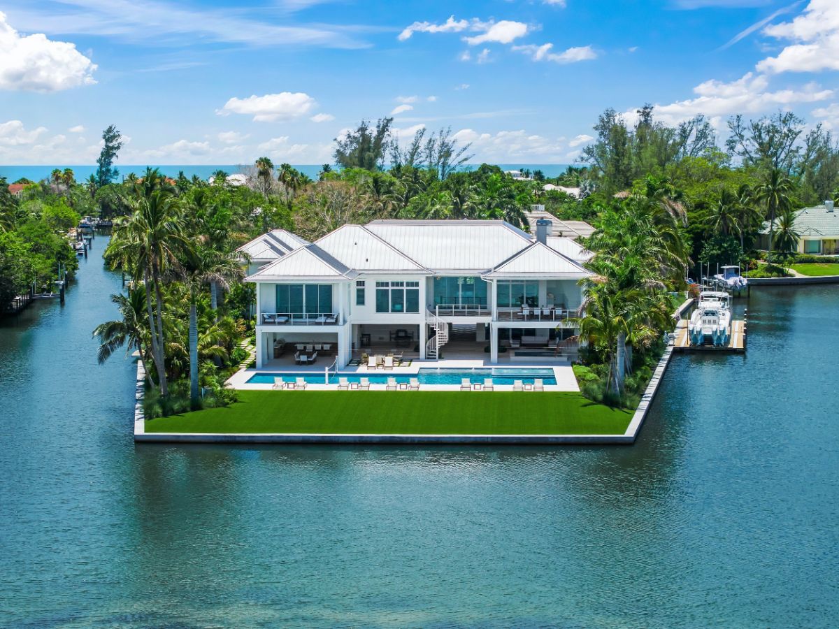 Home is located on a point lot surrounded by water on three sides. Pool deck stretches along the rear with lounge seating facing the bay.
