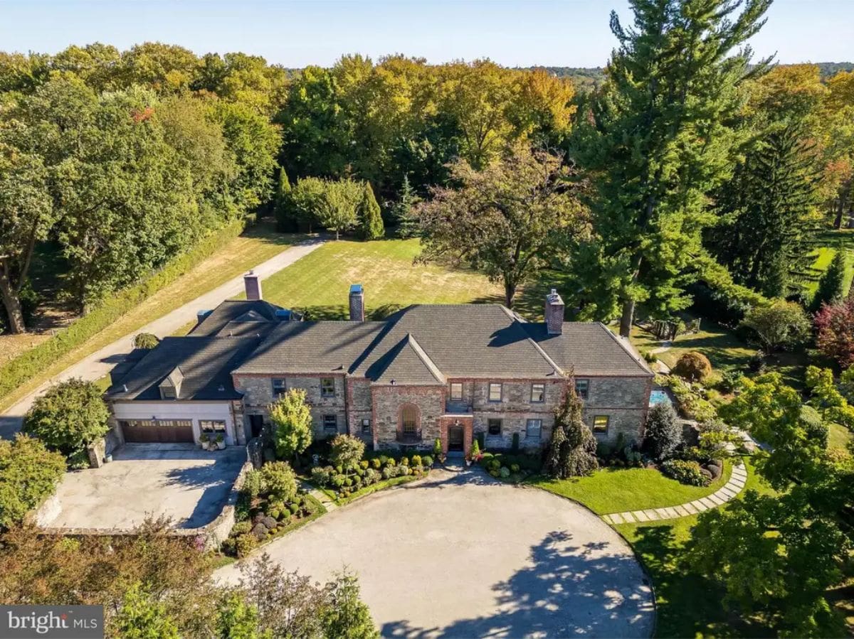 Large two-story stone home is surrounded by mature trees and manicured landscaping.