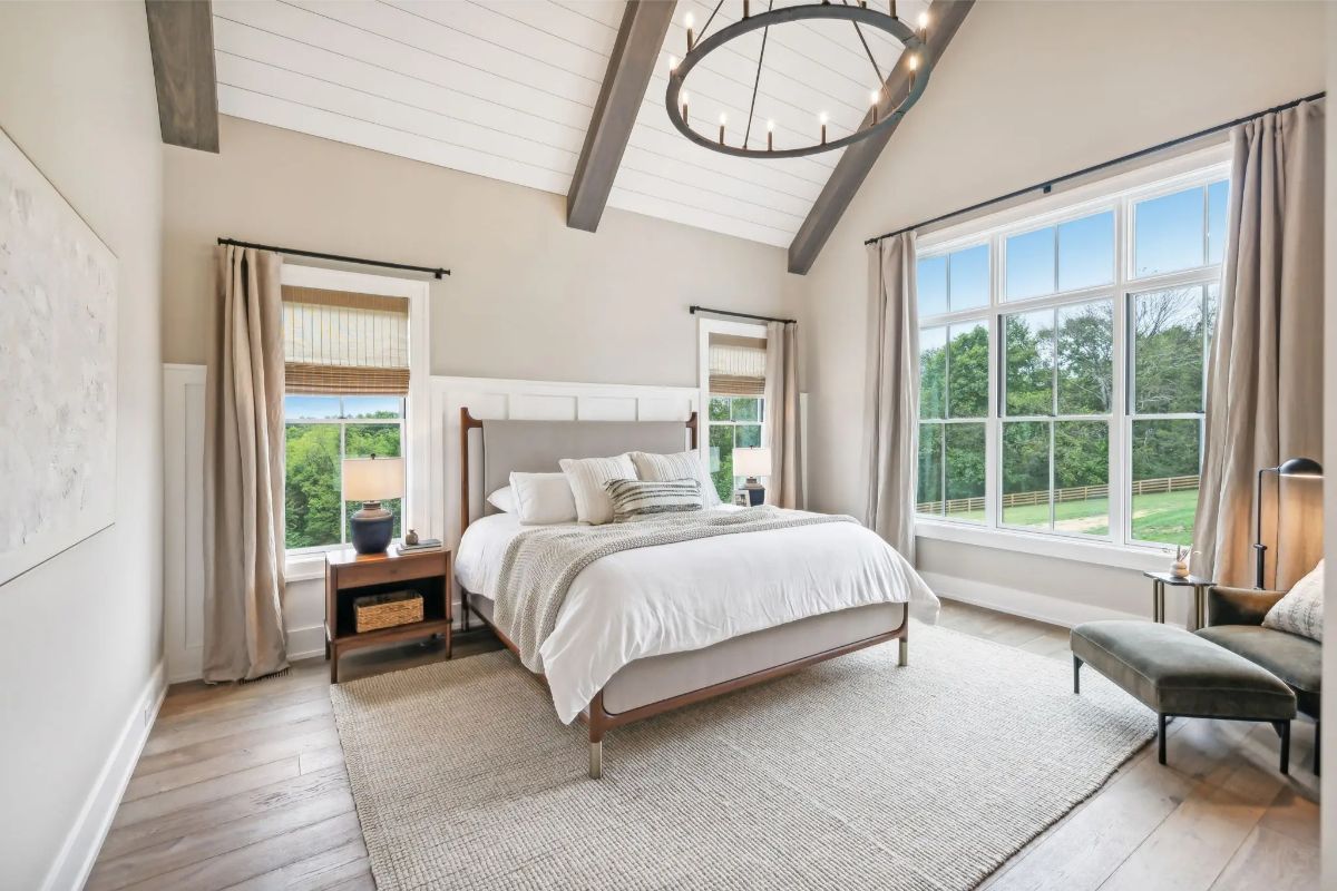 Vaulted primary bedroom with wood beams, oversized window, and serene countryside views. 