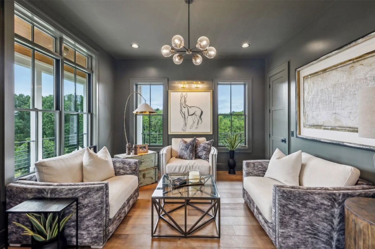 Moody sitting room with dark walls, designer lighting, and plush seating framed by tall windows. 