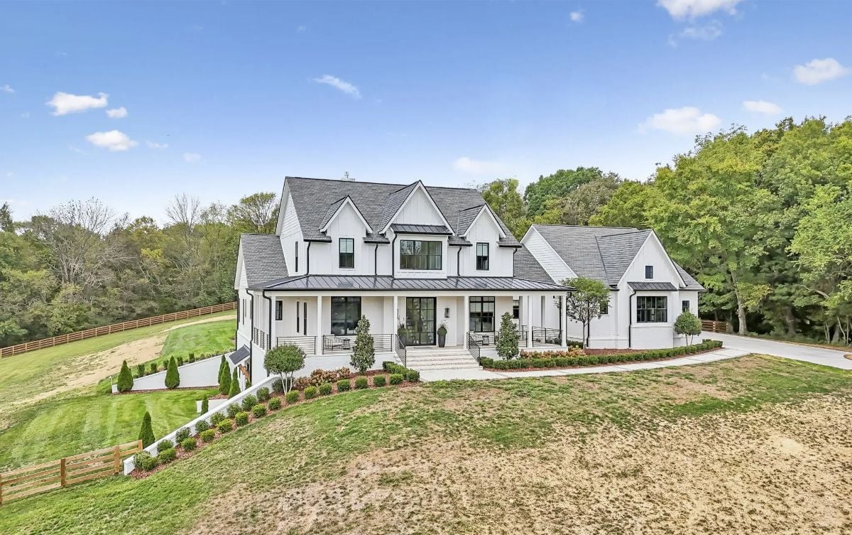 Front exterior of a modern farmhouse-style home with gabled rooflines and expansive front porch. 