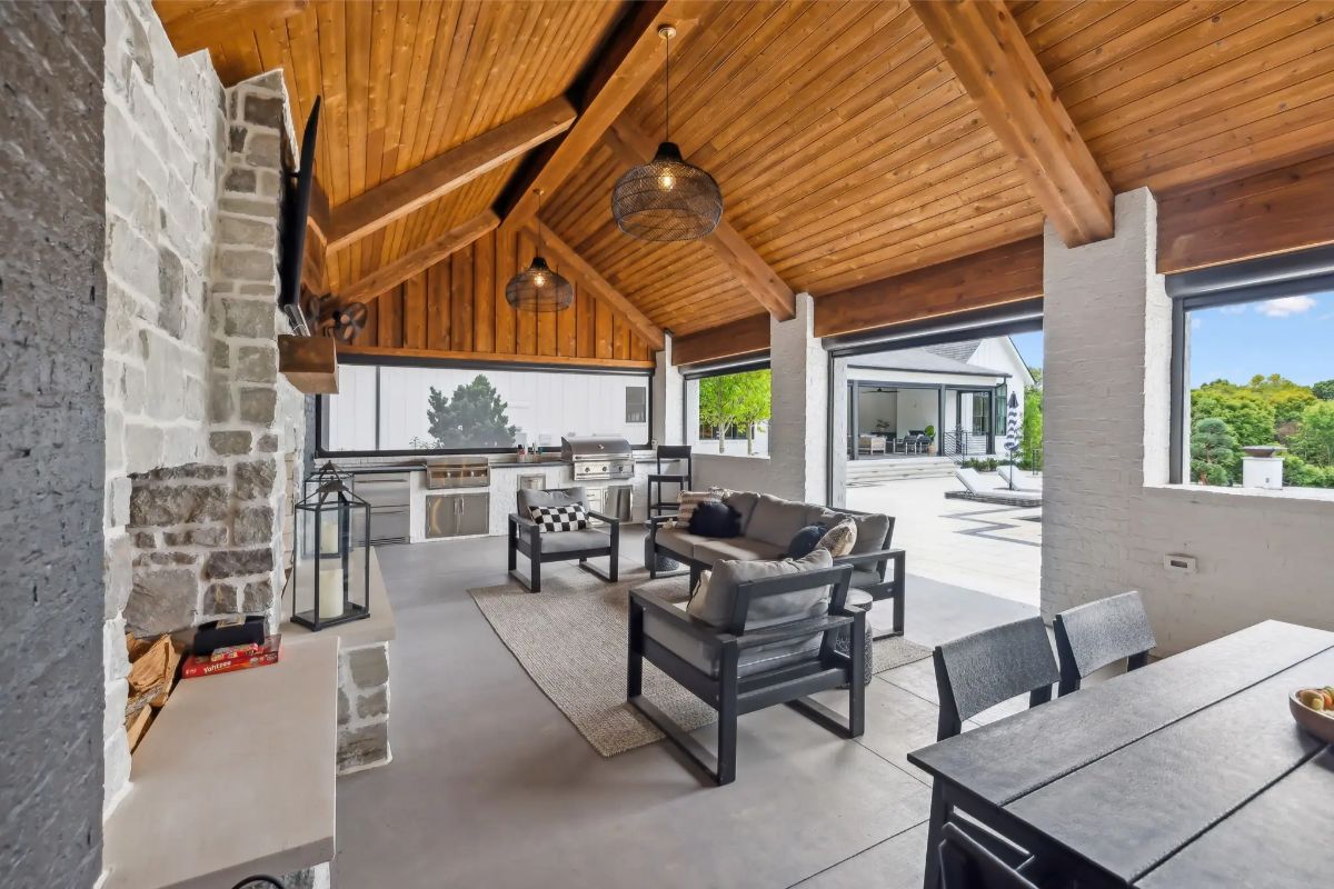 Covered outdoor lounge and kitchen area with vaulted wood ceiling, stone fireplace, and dining space. 