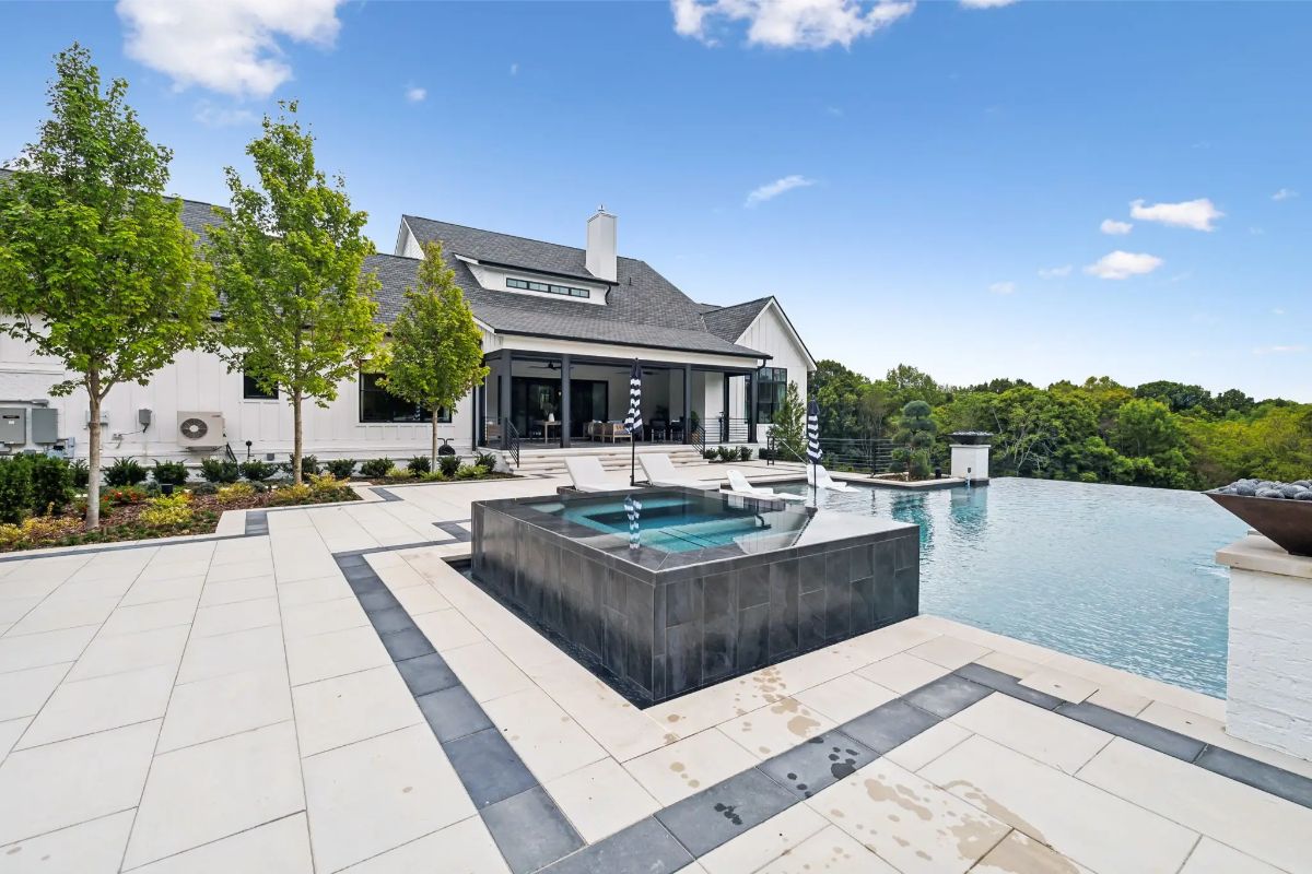 Sleek infinity pool and spa surrounded by modern hardscaping and forested views. 