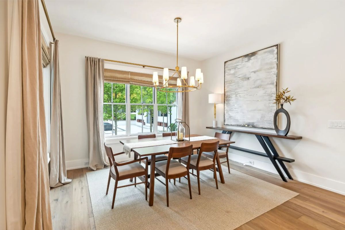 Dining room with mid-century modern furniture, layered lighting, and large windows offering lush outdoor views. 