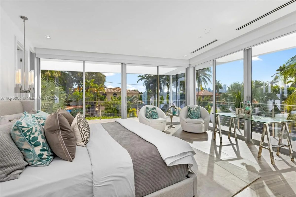 Primary bedroom is surrounded by floor-to-ceiling glass on two sides, offering views of lush landscaping.