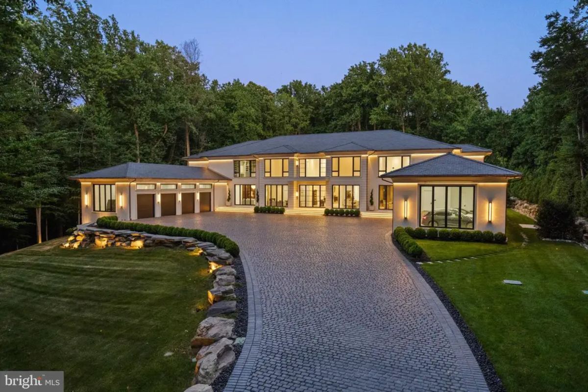 Large contemporary home sits on a manicured lot with a curved cobblestone driveway.