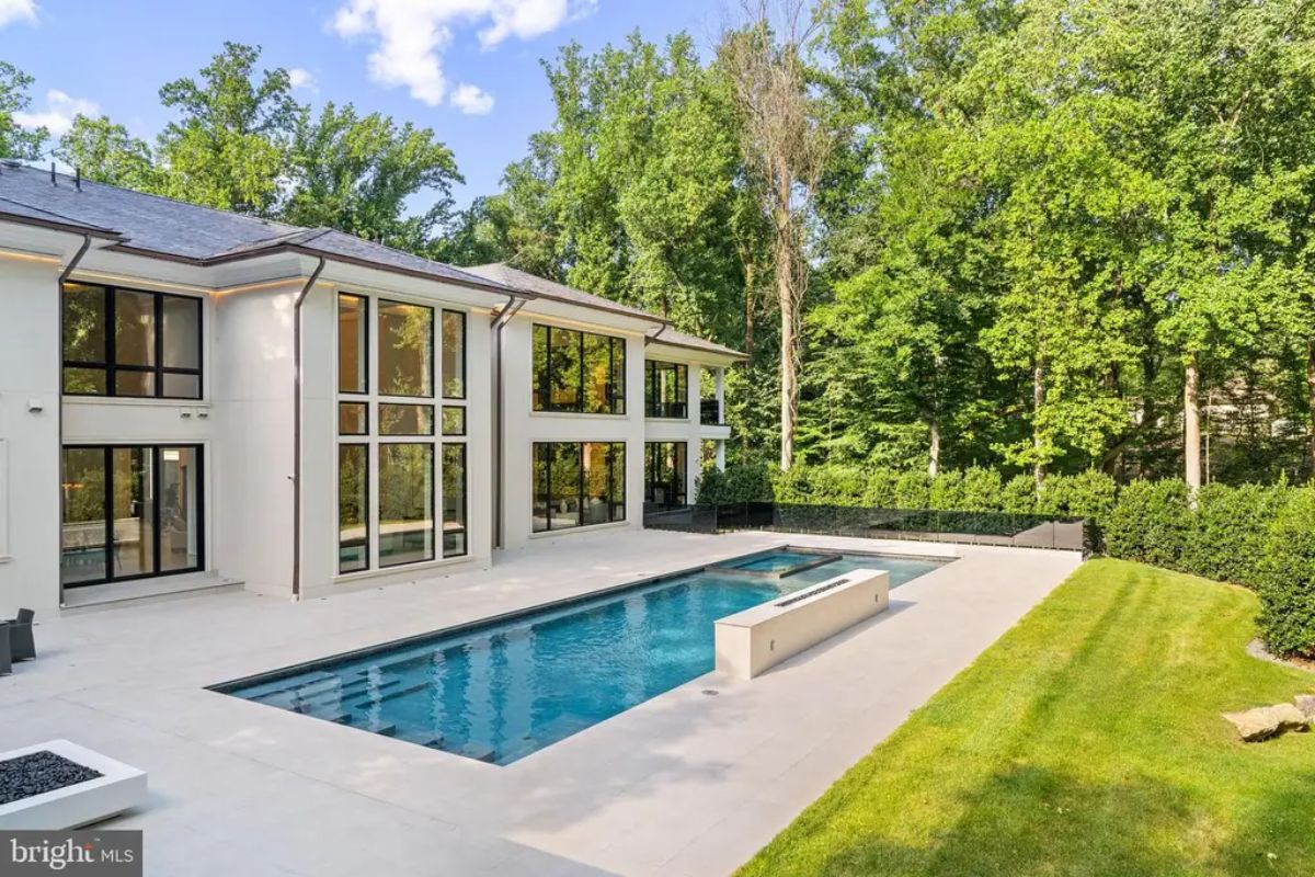 Rectangular swimming pool with built-in fire features sits in the backyard of a modern home.