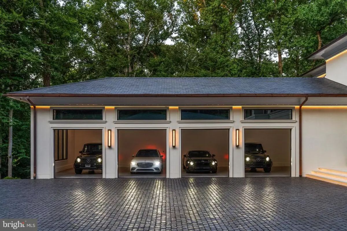 Three-car garage has open doors revealing high-end vehicles parked inside.