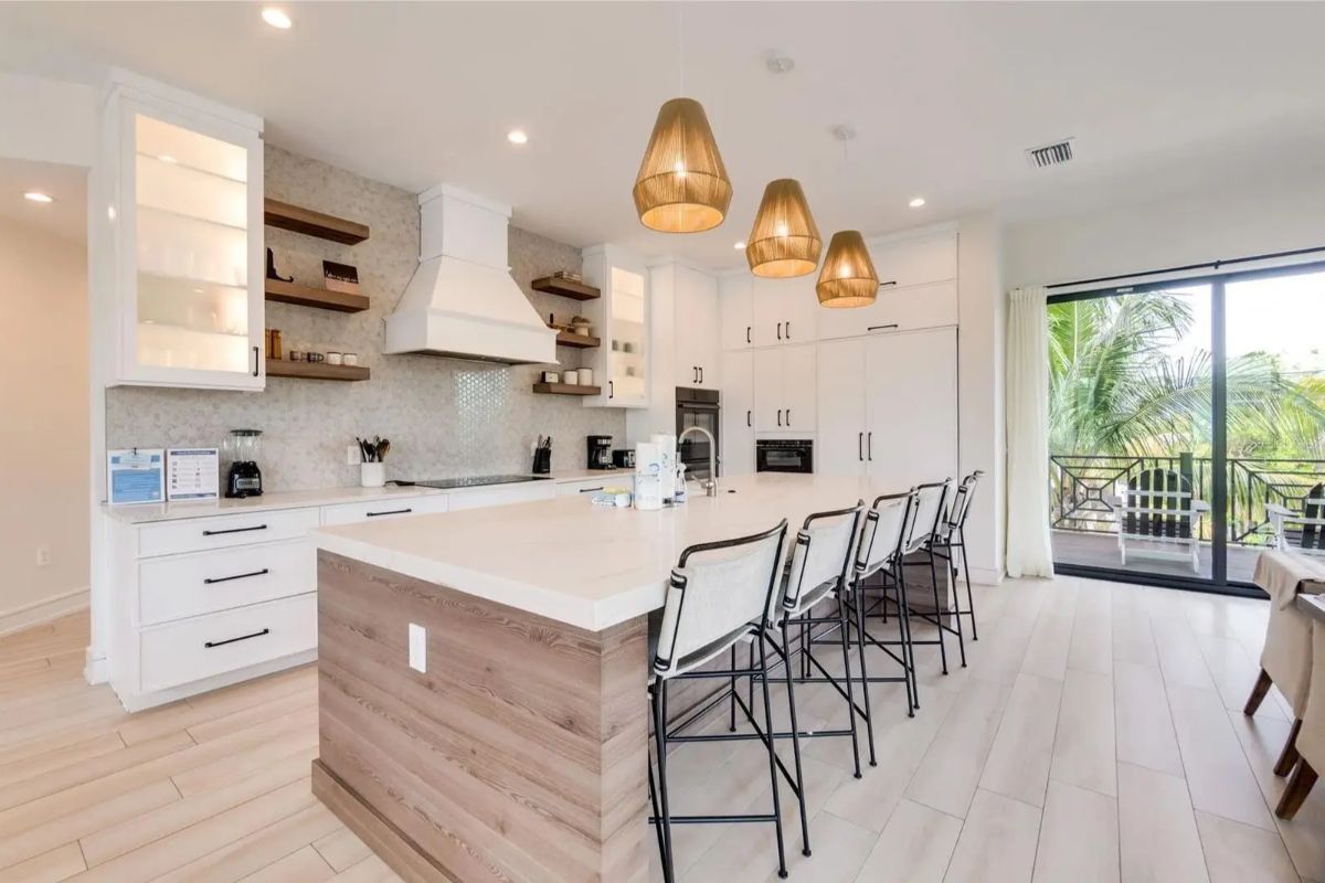 Modern kitchen has white cabinetry, light countertops, and a large island with wood paneling and four bar stools.