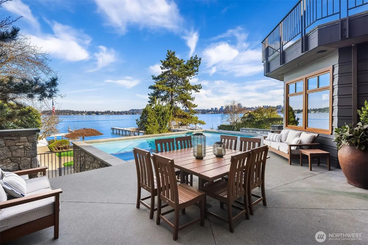 Daytime patio space with a dining table and poolside lounging, all overlooking serene lake scenery. 