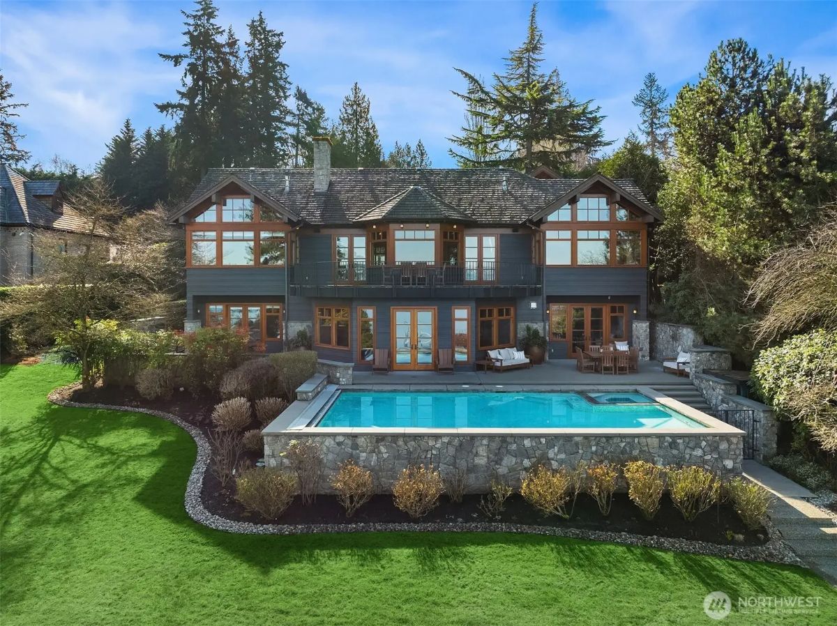 Rear view of the home by day showcasing the stone-trimmed pool, manicured lawn, and timber-accented architecture. 