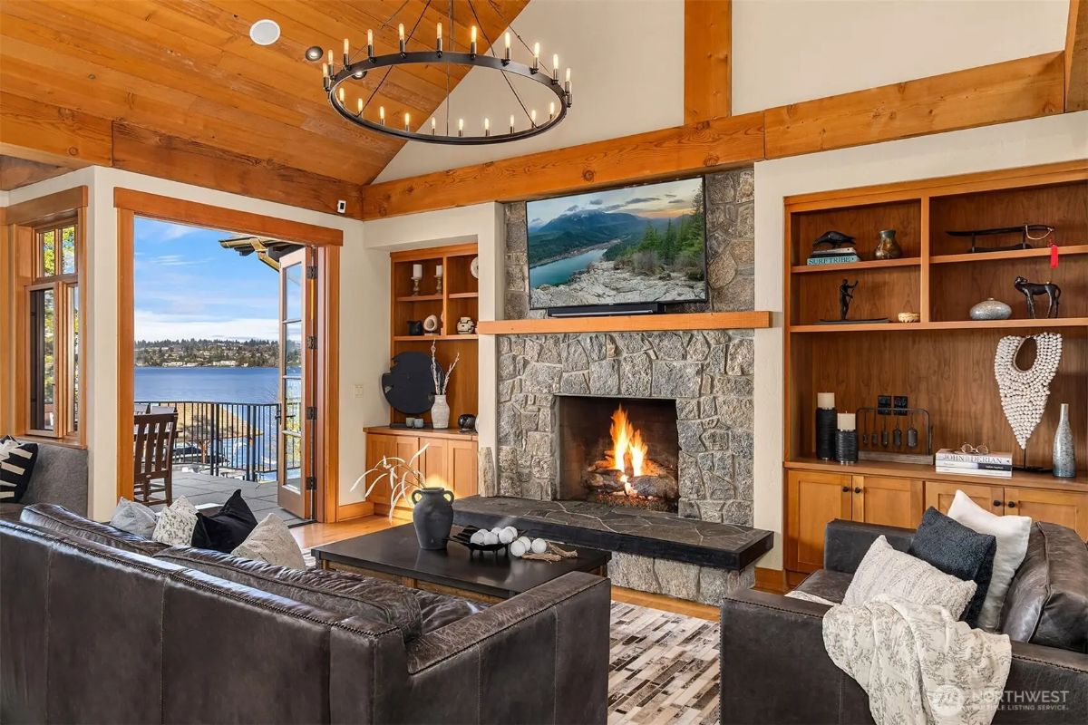 Cozy living area with a rustic stone fireplace, built-in shelving, and serene lake views. 