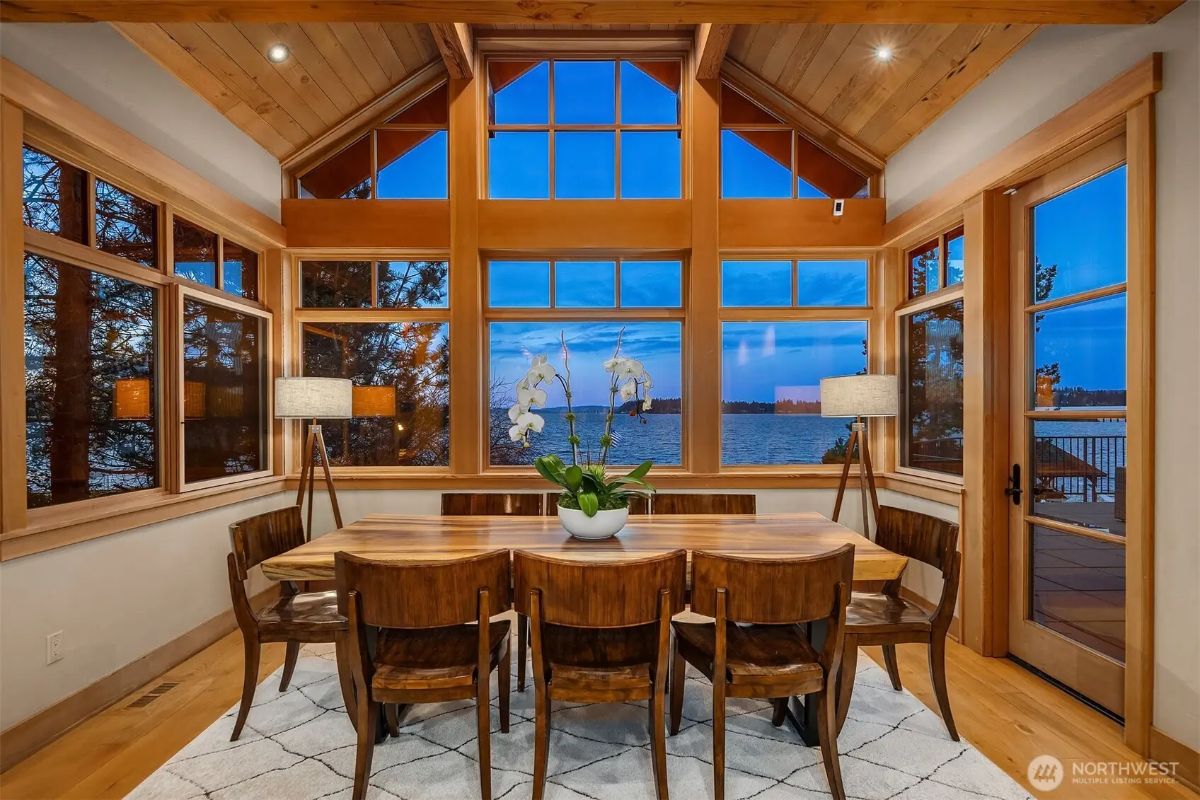 Bright and airy dining nook surrounded by floor-to-ceiling windows framing the water views. 