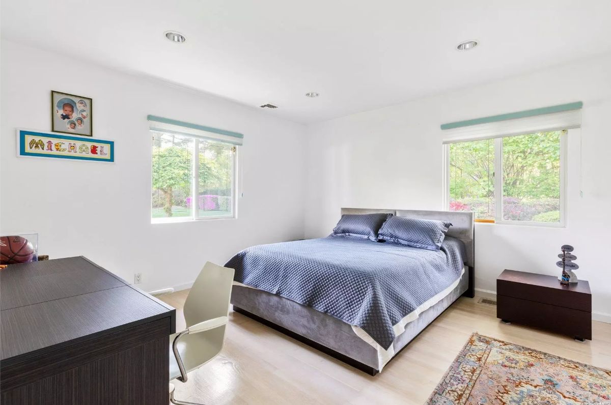 Platform bed with blue bedding is centered between two large windows.