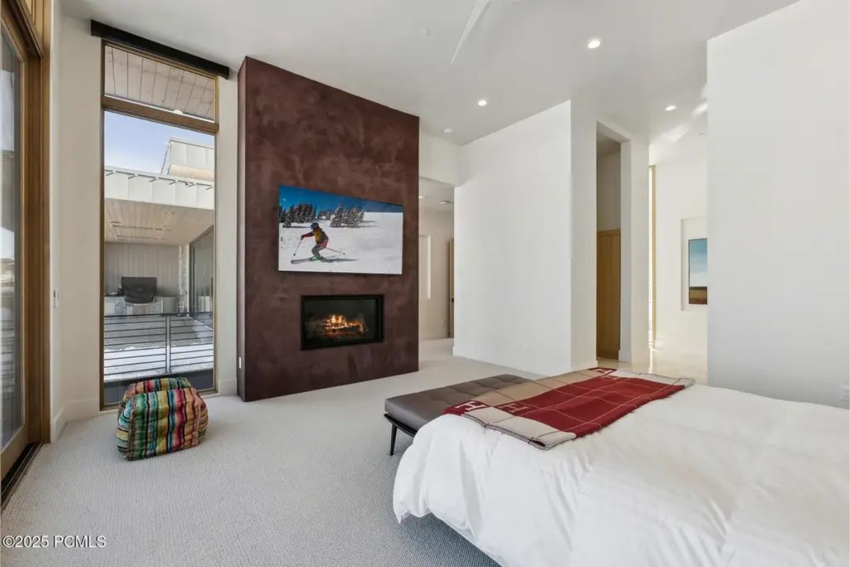 Cozy bedroom with a fireplace, a sleek design, and a mounted TV above the fire, featuring access to a private terrace. 