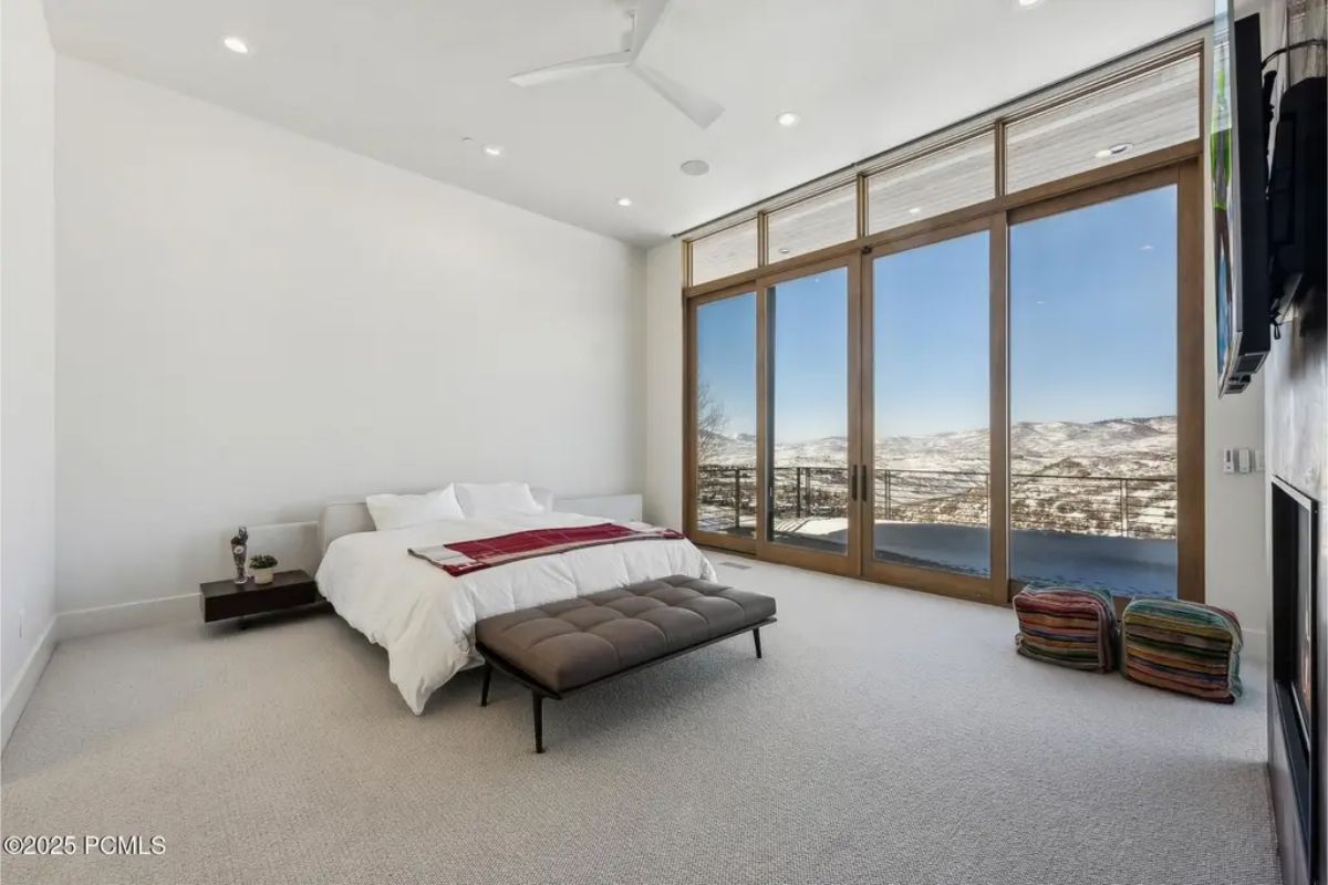 Minimalist bedroom with floor-to-ceiling glass doors opening to a stunning mountain landscape. 