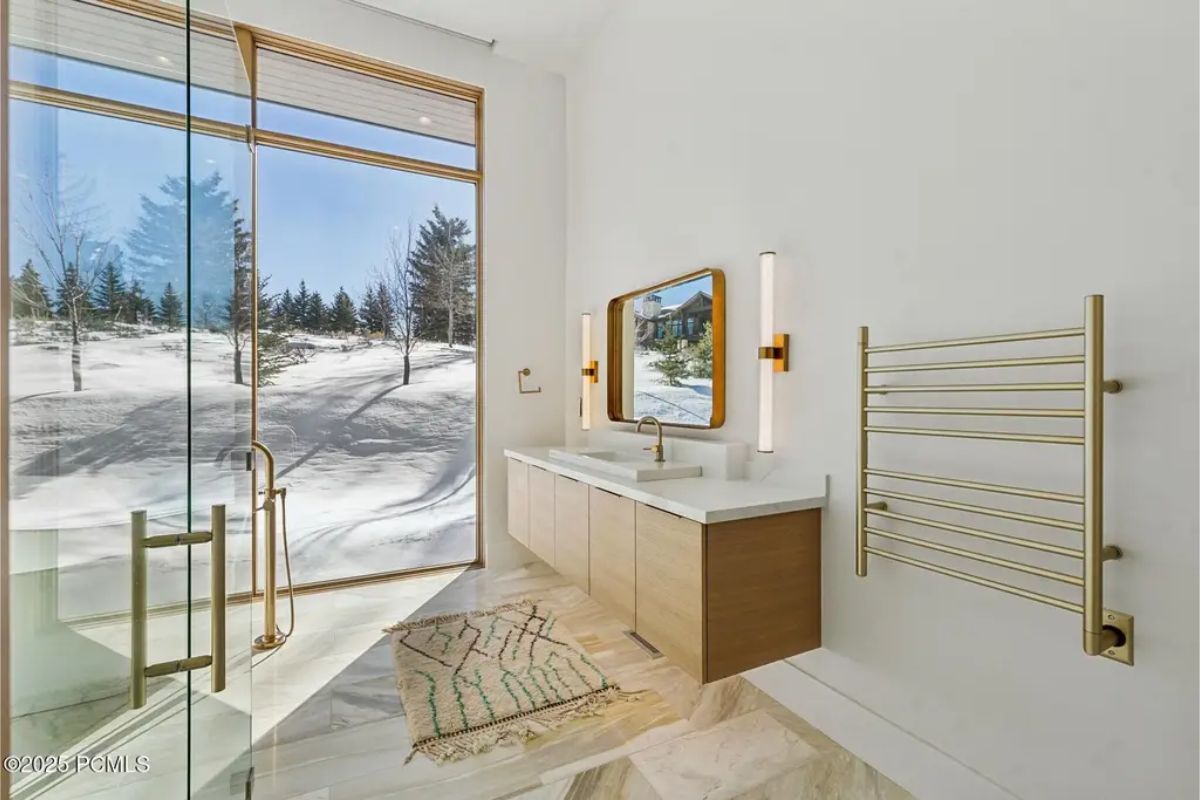 Bathroom with floor-to-ceiling windows showcasing snowy views, a modern vanity, and a heated towel rack. 