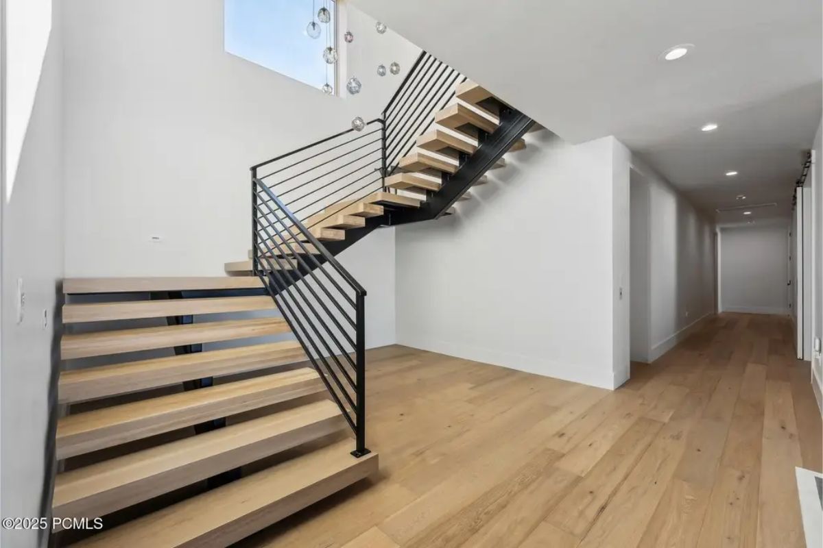 Floating wooden steps and metal railings create a stylish modern staircase leading to a sleek hallway. 