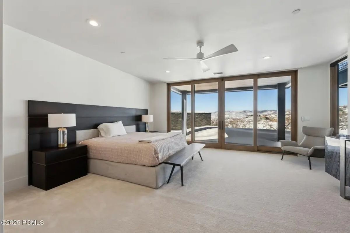 Spacious bedroom with a modern black bed frame, a ceiling fan, and large glass doors leading to an outdoor balcony with scenic views. 