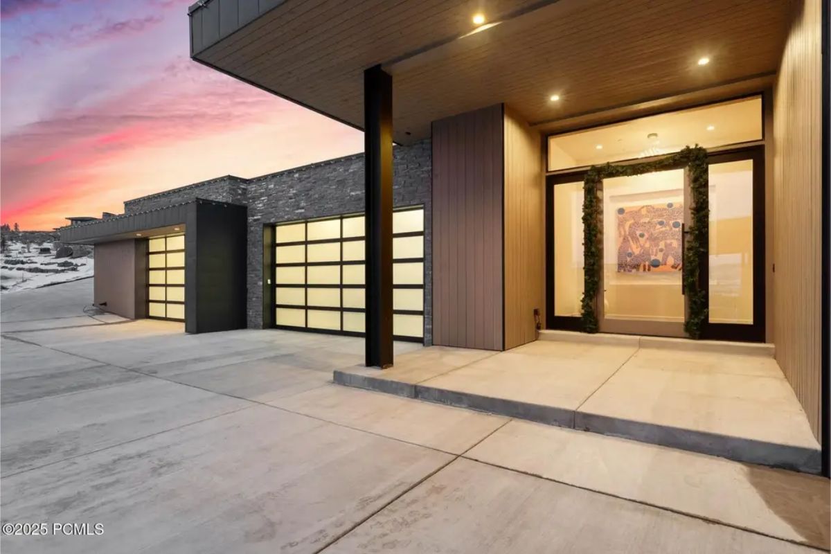 Front entrance features large glass-paneled garage doors, a minimalist design, and soft ambient lighting. 