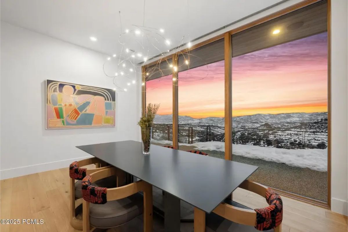 Dining room showcases a black table, modern chairs, and an uninterrupted sunset-lit landscape beyond the glass walls. 