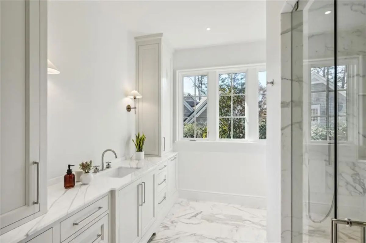 Bright and timeless bathroom with marble flooring and clean white cabinetry. 
