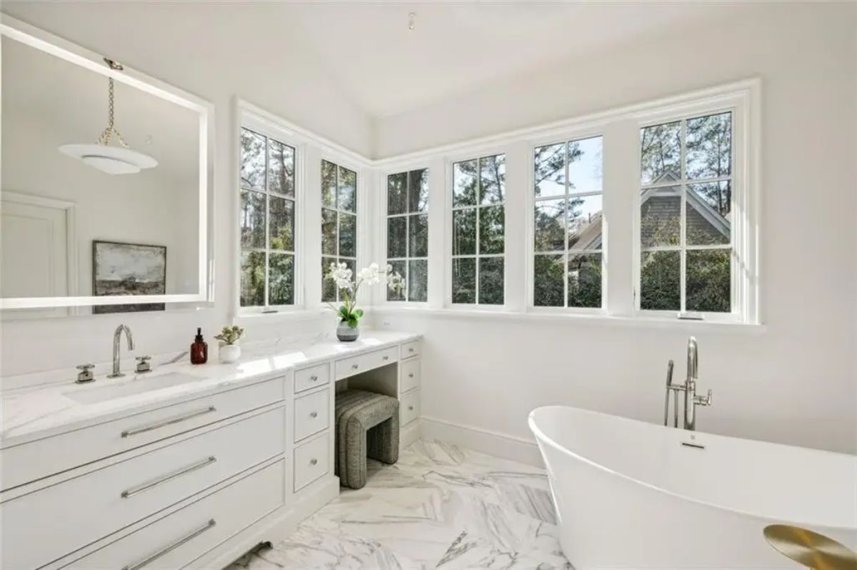 Corner vanity and soaking tub framed by panoramic windows in a serene spa-like bathroom. 