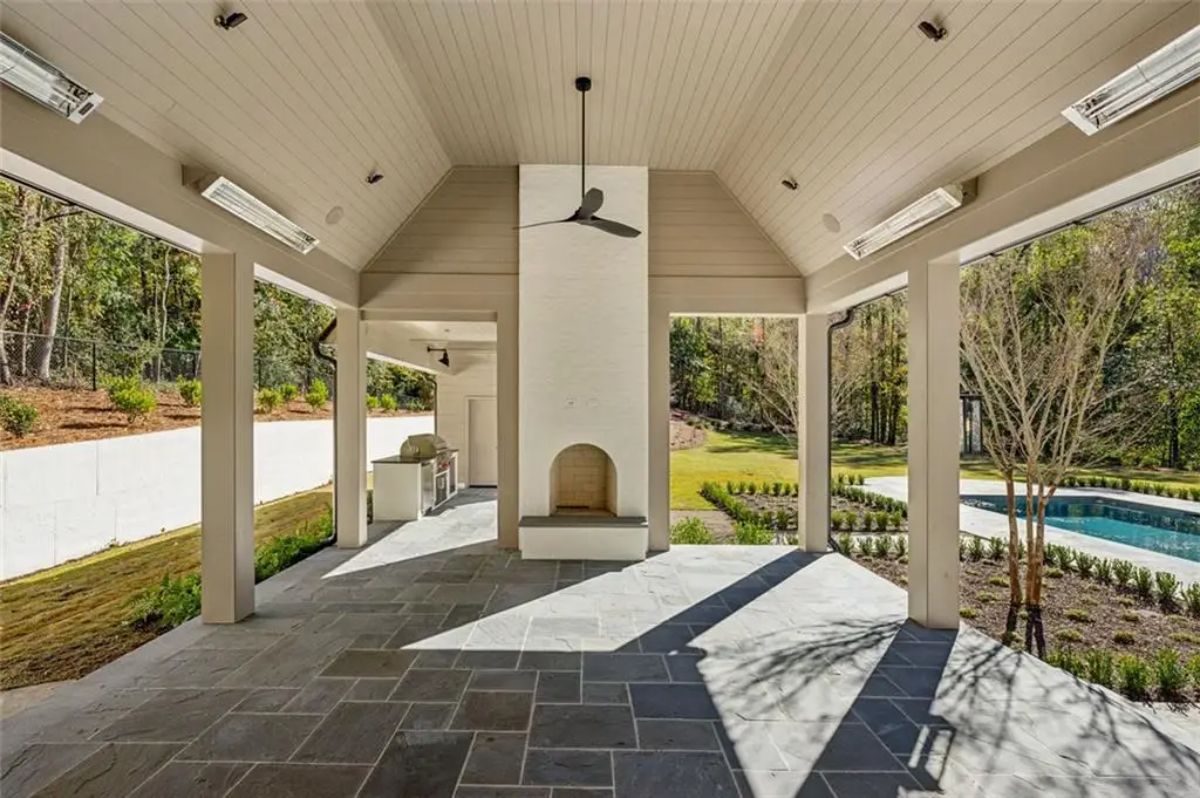 Covered outdoor lounge with a modern fireplace and ceiling fan opens to the backyard and pool. 