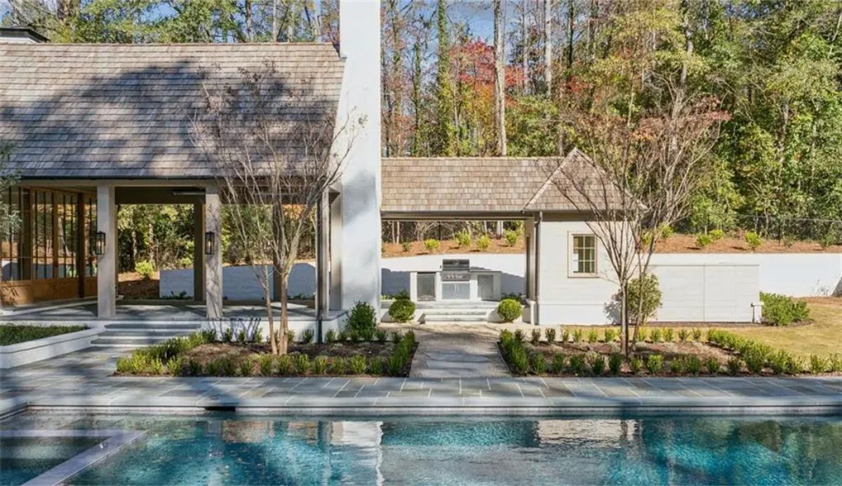 Poolside view of a sleek guest house with a central chimney and manicured landscaping. 