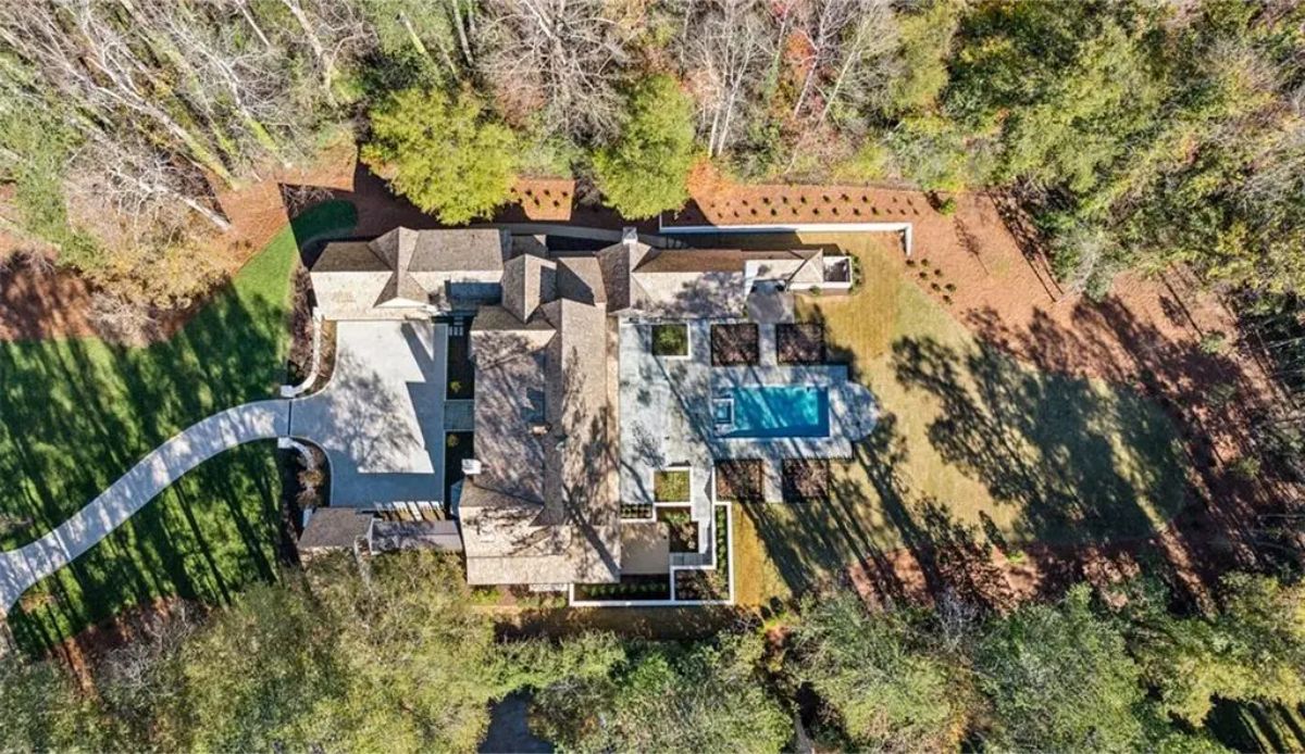 Top-down view of the full estate nestled in the woods with a long driveway and central pool. 