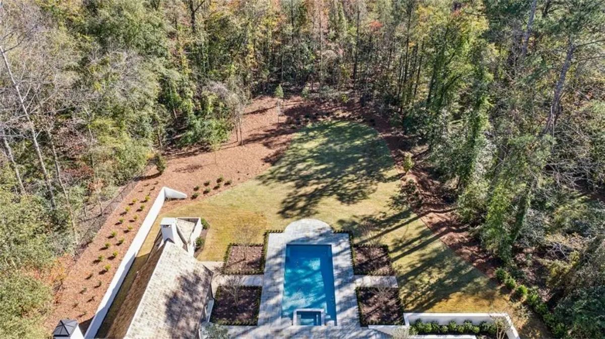 Aerial shot of the backyard showing a pool area surrounded by forest and manicured lawn. 