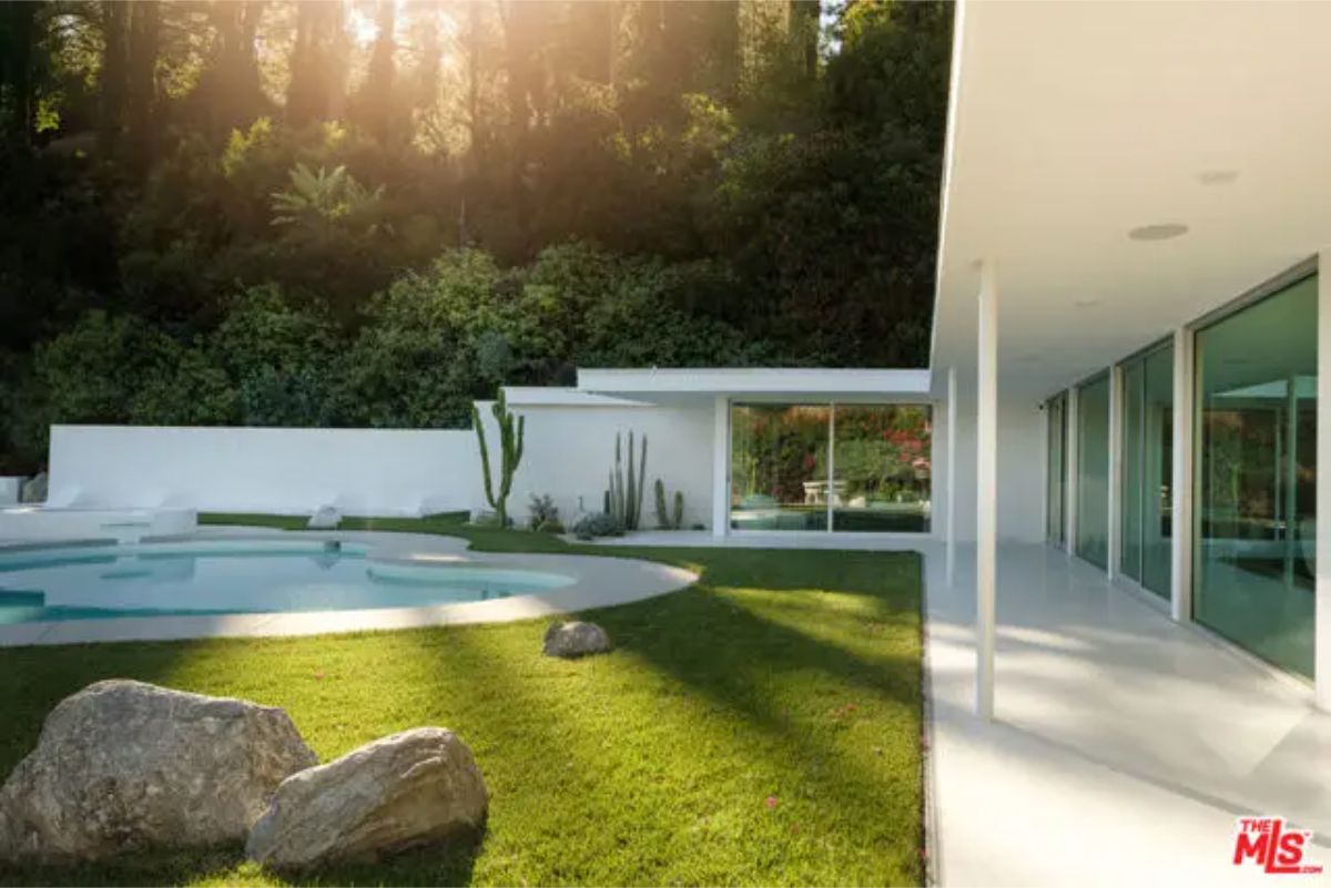 Stunning backyard with a lush green lawn, modern architecture, and a serene poolside retreat. 